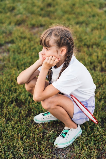 青い草の上でうずくまるバドミントンの悲しい少女