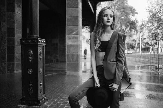 Sad girl with a hat standing in the street. Fashion model in the city. Fit lady with a long hair street fashion. Stylish woman wearing siut