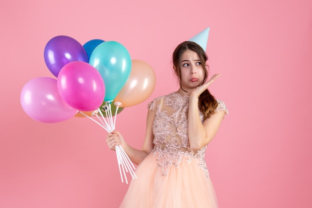 sad girl with party cap holding balloons on pink