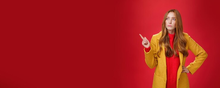 Free Photo sad and gloomy cute ginger girl in s wearing trendy yellow coat holding hand on waist pouting lookin