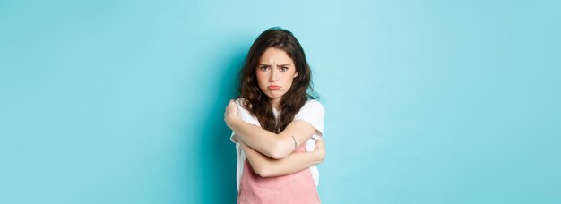 Sad and gloomy young woman pouting comforting herself with cuddles hugging her body and looking upse