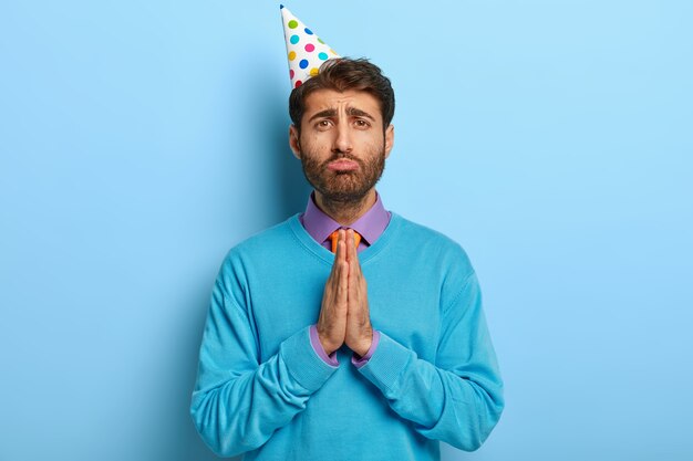 Грустный парень в шляпе на день рождения позирует в синем свитере