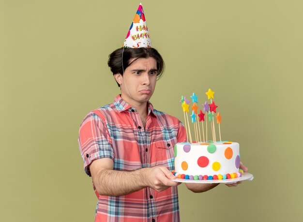 생일 모자를 쓰고 슬픈 잘 생긴 백인 남자가 생일 케이크를 보유하고 보인다.