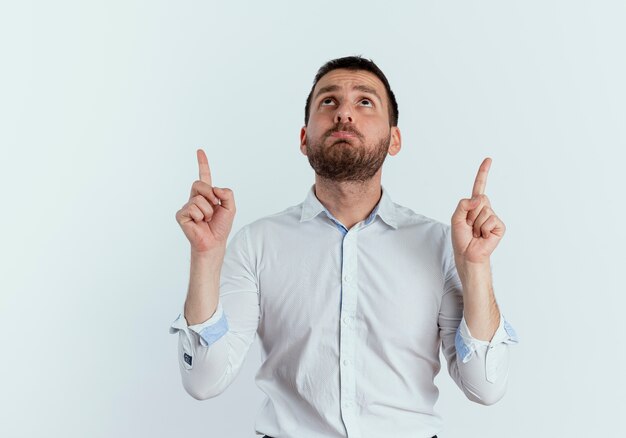 Sad handsome man looks and points up with two hands isolated on white wall