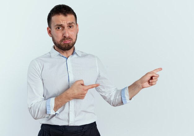 Sad handsome man points at side with two hands isolated on white wall