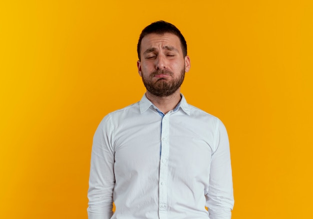 Sad handsome man stands with closed eyes isolated on orange wall