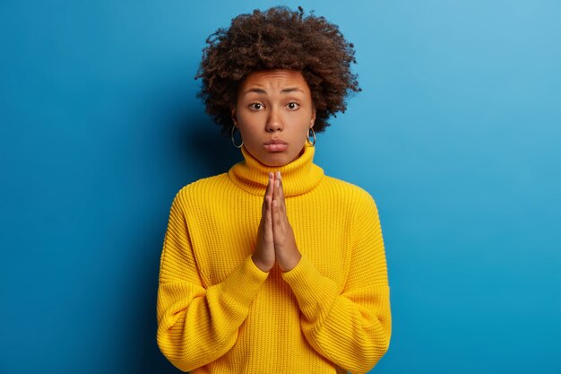 sad hopeful woman with curly hairdo holds hands pressed together as sign of hope, makes praying gesture, needs support and help