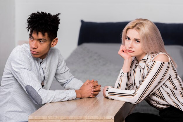 Sad interracial young couple sitting face to face looking away