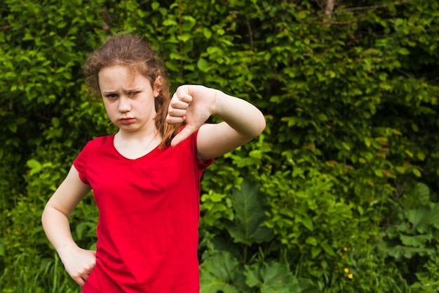 Sad little girl showing dislike gesture in park