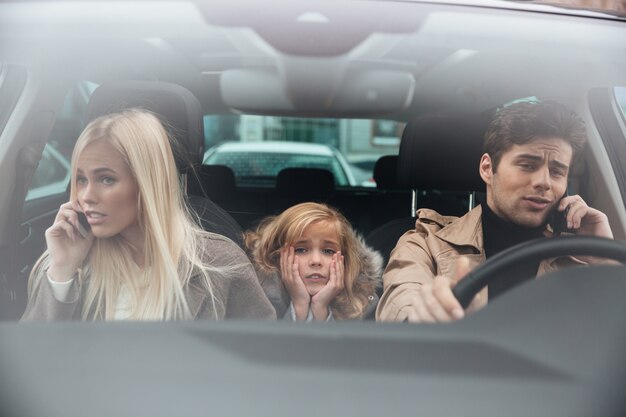 Sad little girl sitting in car while her parents talking