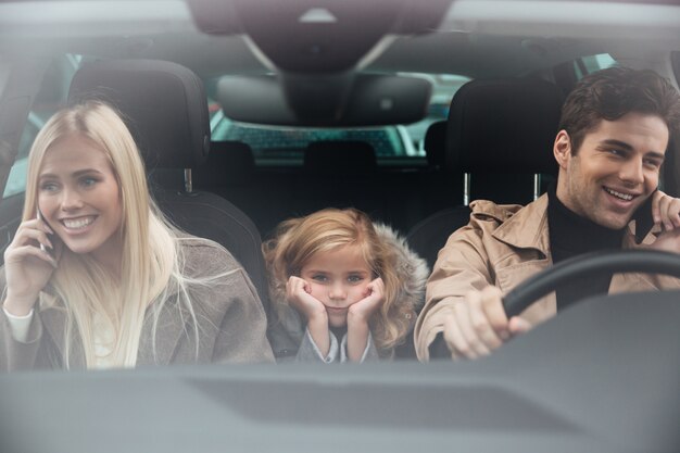 Sad little girl sitting in car while her parents talking