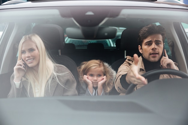 Грустная маленькая девочка сидит в машине, пока ее родители разговаривают