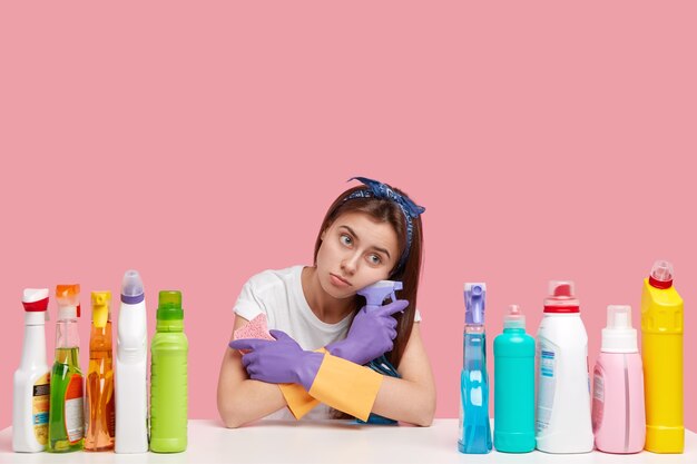 Sad lonely woman with displeased expression, tired fatigue look, carries washing spray, sponge, dressed in casual clothes