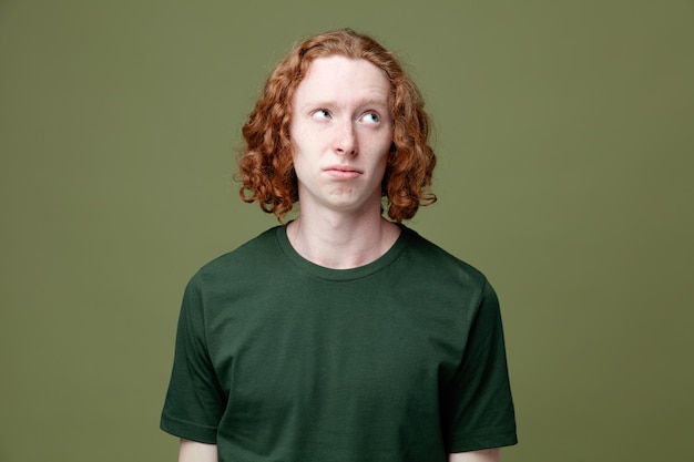 Sad looking at side young handsome guy wearing green t shirt isolated on green background