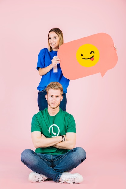 Sad man sitting in front of happy woman holding winking emoji speech bubble