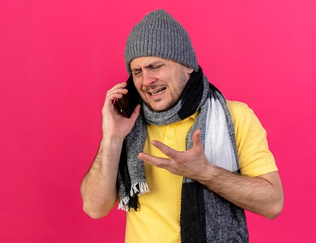 Sad man waring winter hat and scarf talks on phone on pink