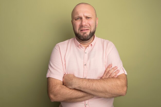 Sad middle-aged bald man wearing pink t-shirt crossing hands