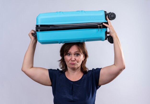 Free photo sad middle-aged traveler woman holding suitcase on head on isolated white