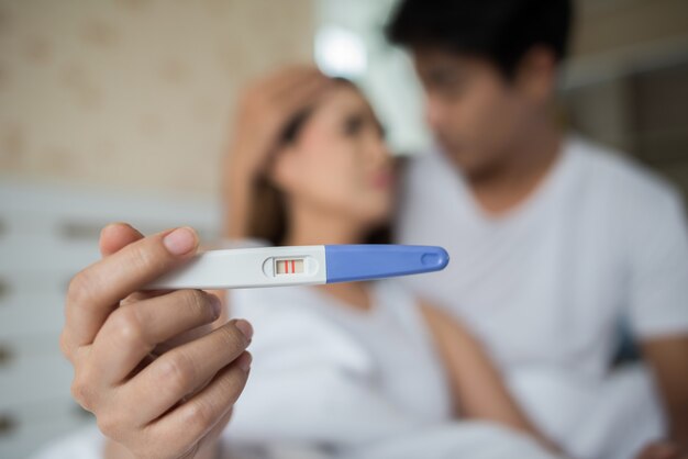 Sad parent complaining holding a pregnancy test sitting on bed