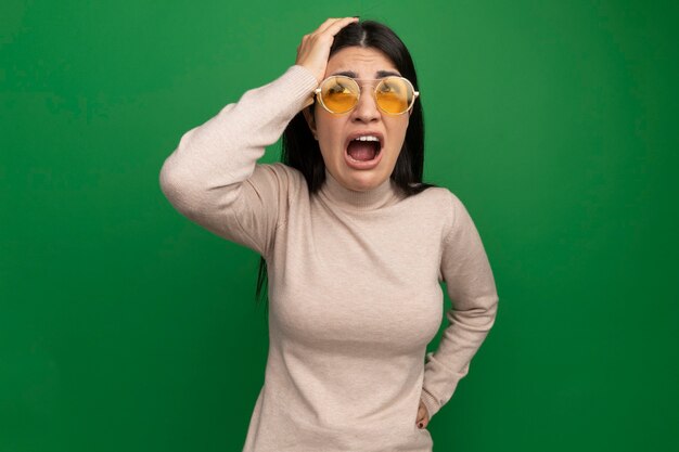 Free photo sad pretty brunette caucasian girl in sun glasses puts hand on head and looks up on green