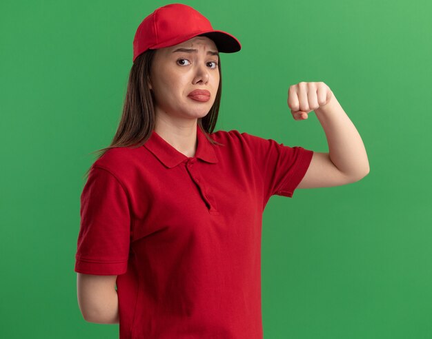 Sad pretty delivery woman in uniform keeps fist