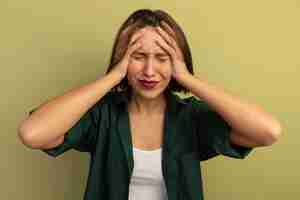 Free photo sad pretty woman holds head isolated on olive green wall