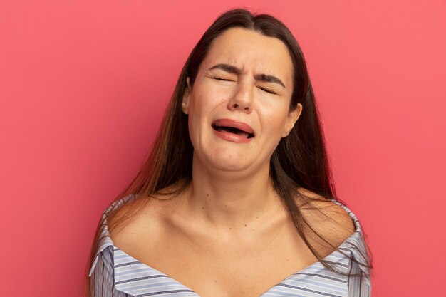 Sad pretty woman pretends to cry isolated on pink wall