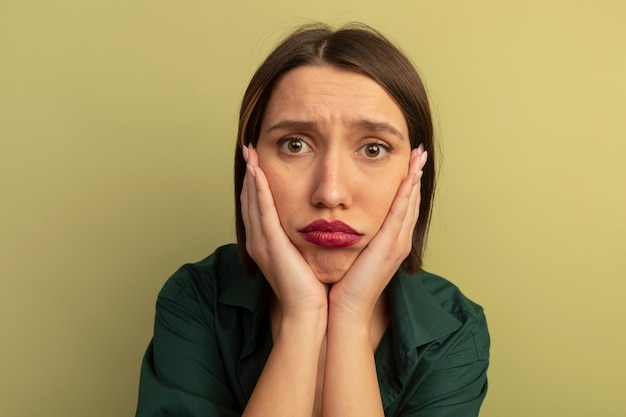 Sad pretty woman puts hands on face isolated on olive green wall