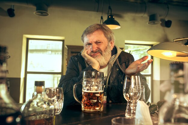 Печальный старший мужчина пьет алкоголь в пабе