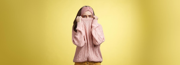 無料写真 悲しい愚かな悲観的なかわいい若い女の子がセーターの襟に顔を隠して、鼻にしかめっ面の disp で服を引っ張る