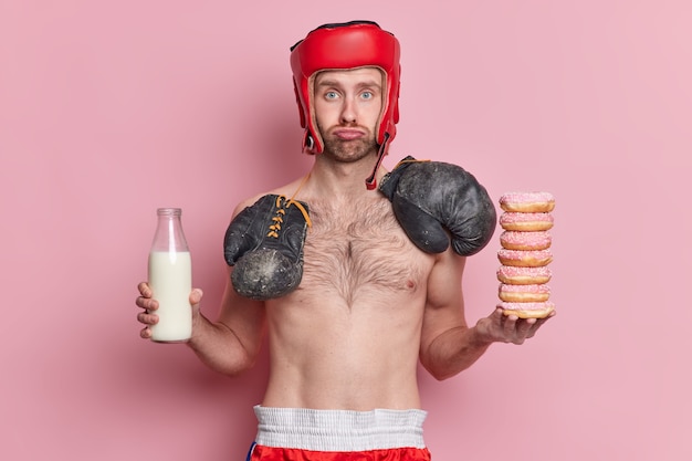 Бесплатное фото Грустный тощий мужчина-боксер носит шляпу, а на шее сидит боксерская роща, держит кучу пончиков и бутылку молока.