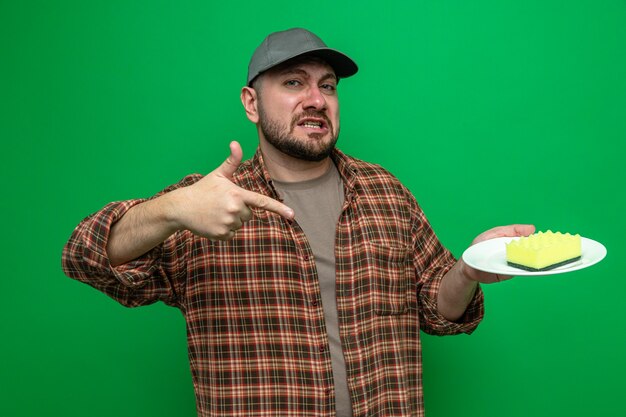 Sad slavic cleaner man holding and pointing at sponge on plate 