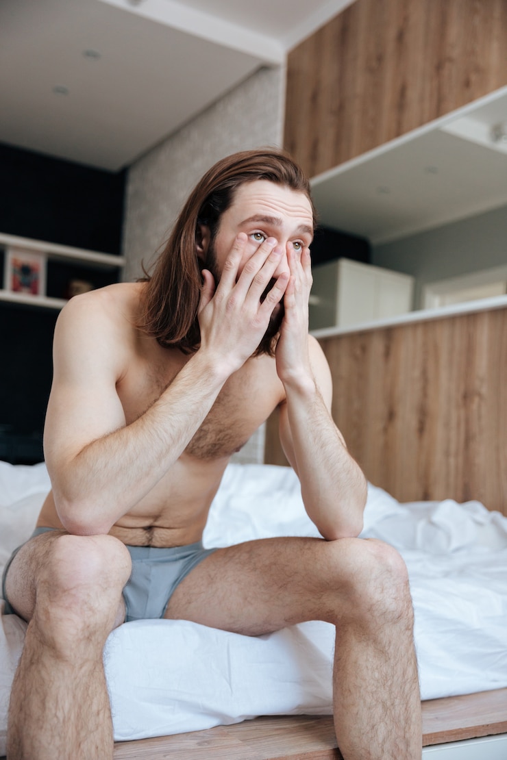 Free Photo sad sleepy young man sitting on bed in the morning