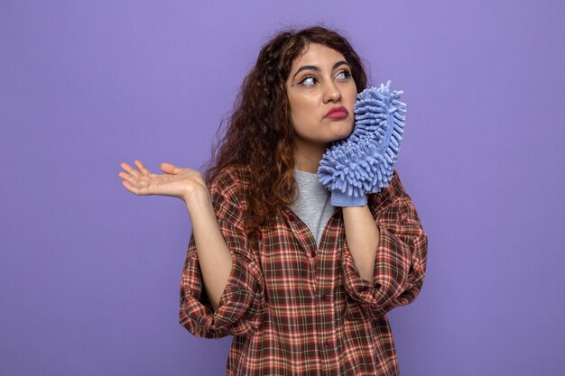 Sad spreading hand young cleaning woman holding cleaning rag 