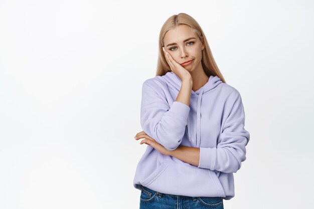 Sad and unamused blond woman smirking looking at camera unimpressed standing bored against white background