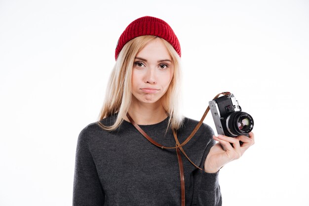 Sad upset girl in hat standing and holding retro camera