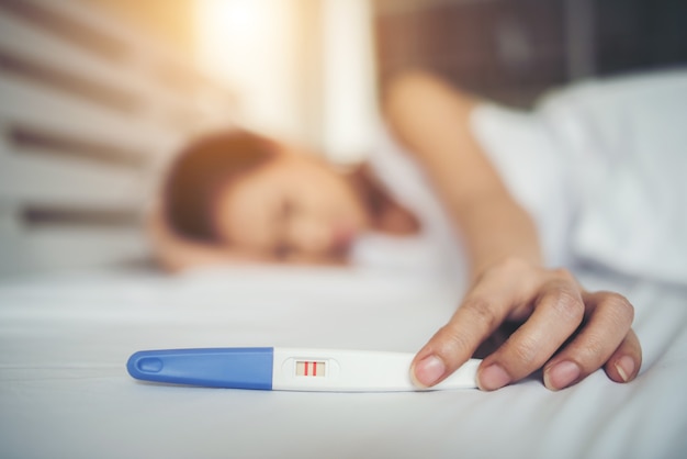 Sad woman complaining holding a pregnancy test sitting on bed