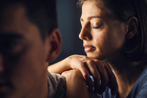Sad woman crying with eyes closed while leaning on boyfriend's shoulder