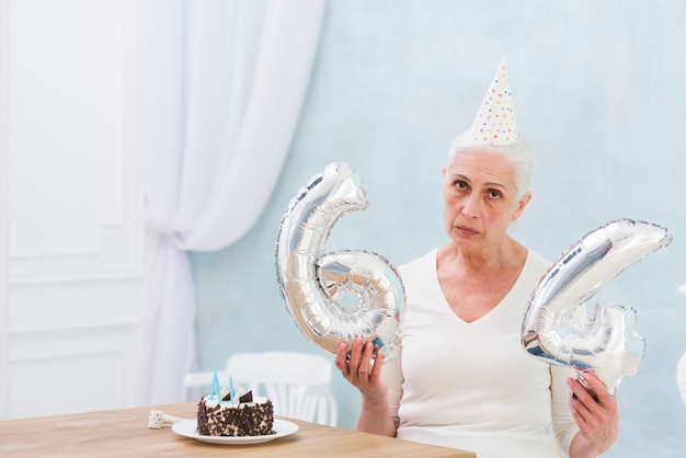 Sad woman holding foil balloon with cake on wooden table