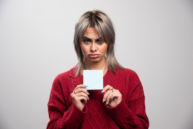 Sad woman holding memo pad on gray background.