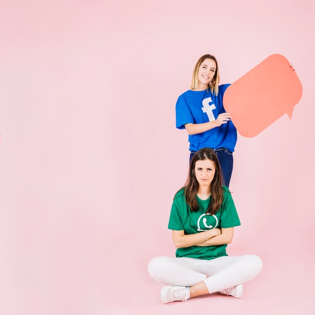 Sad woman sitting in front of her happy friend holding speech bubble