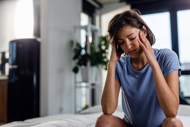 Foto gratuita donna triste che soffre di mal di testa e si siede sul letto con gli occhi chiusi mentre si tiene la testa dolorante