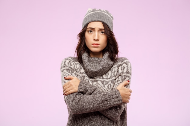 Sad young beautiful girl feeling cold over light wall