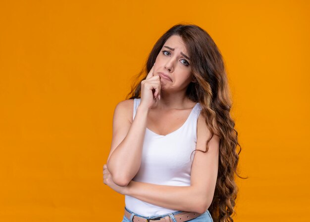 Sad young beautiful girl putting hand on chin on isolated orange space with copy space