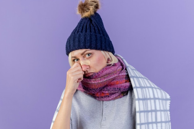 冬の帽子とスカーフを身に着けている鼻に医療絆創膏で悲しい若いブロンドの病気のスラブ女性