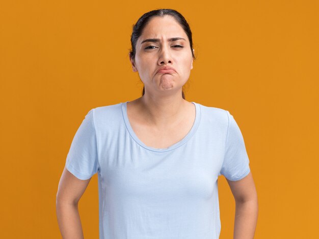 Sad young brunette caucasian girl  isolated on orange wall with copy space