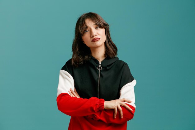 Sad young caucasian woman keeping arms crossed looking at camera isolated on blue background