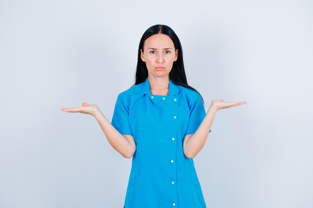 Sad young dcotor is looking at camera by opening wide her hands on white background