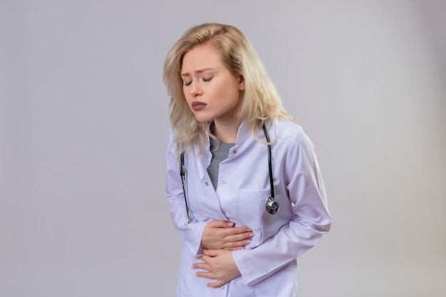 Free photo sad young doctor wearing stethoscope in medical gown grabbed aching stomach on white wall