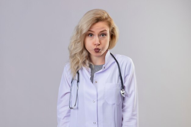 Sad young doctor wearing stethoscope in medical gown on white wall